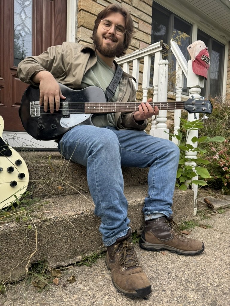 Chase sitting on porch steps playing a bass guitar