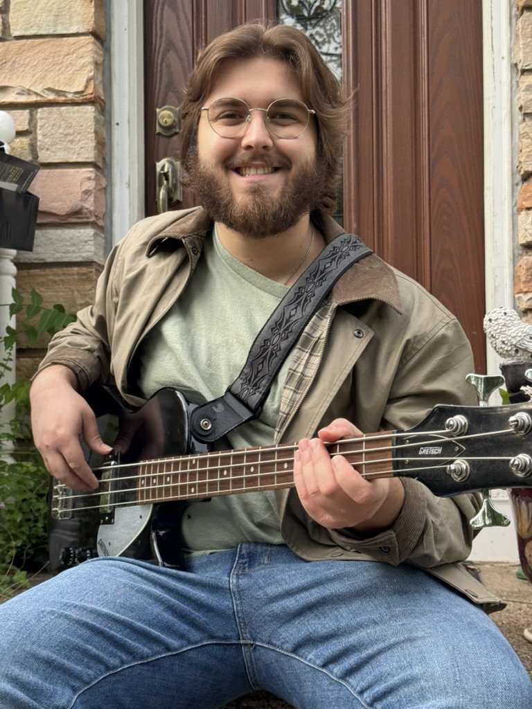 Chase smiling with a bass guitar in front of a wooden door